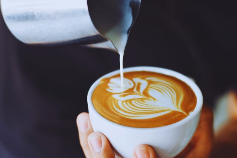 A person making latte art in a cup of coffee with steamed milk.